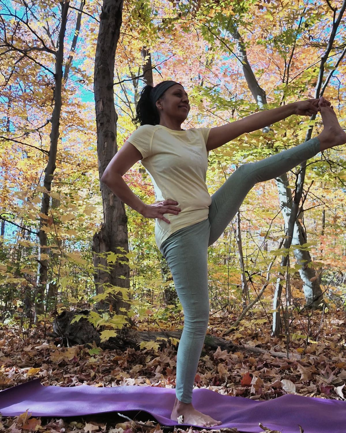 Sneh Lata holding a standing leg extension on a forest floor